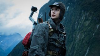 a woman in rain jacket stands near a mountain