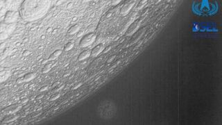 black and white image of the moon's cratered surface, with a blurry and distant earth in the background