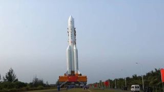 a white rocket rolls down a road on its transporter with a blue sky in the background